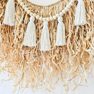 Natural straw, Raffia hanging with wood beaded garland of cotton tassels. Coastal Bohemain, boho inspired home. Coastal boho interior style wall hangings. Natural wall art. Natural earrhy organic materials. 